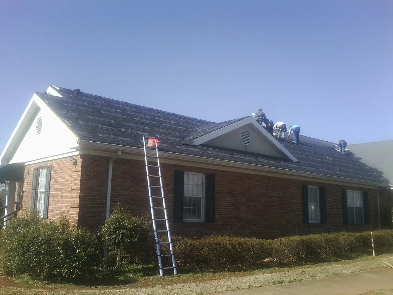 Crew tearing shingles off a brick ranch roof with a ladder set — Metal Roof Repair work by our crew in Smyrna
